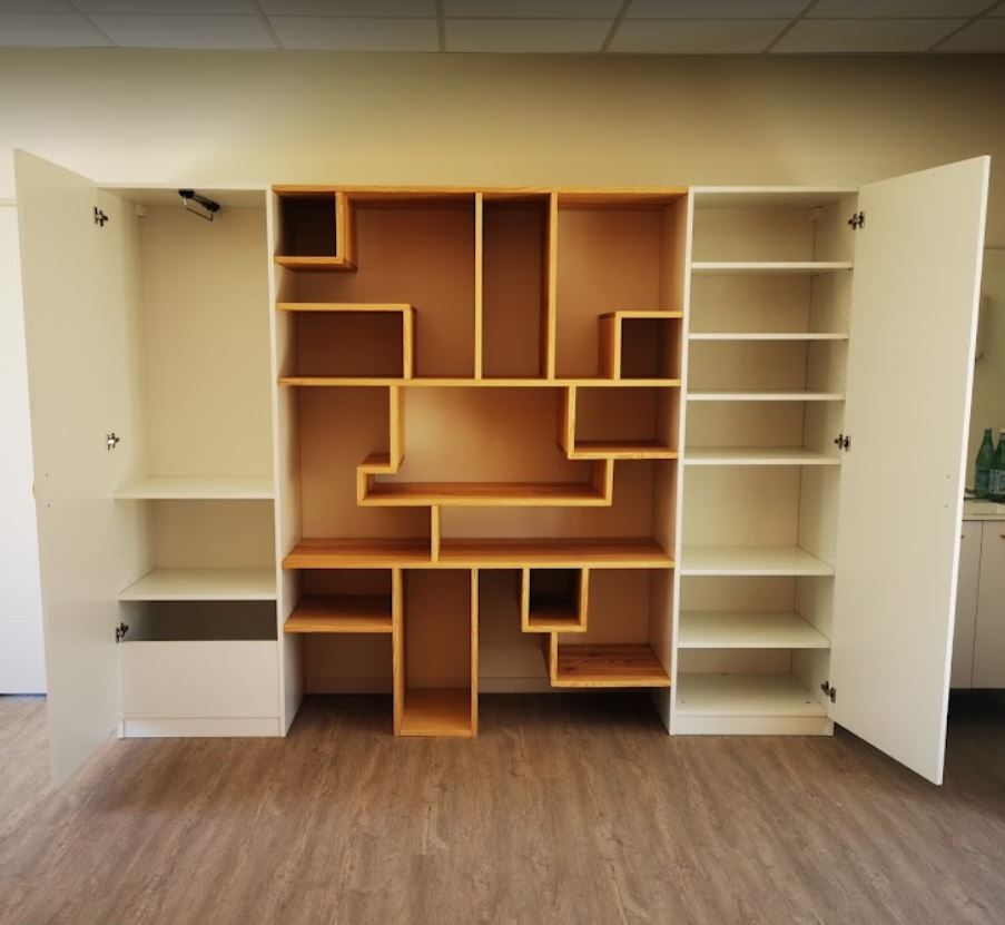 Bibliothèque murale aux niches de bois asymétriques, encastrée entre deux penderies.