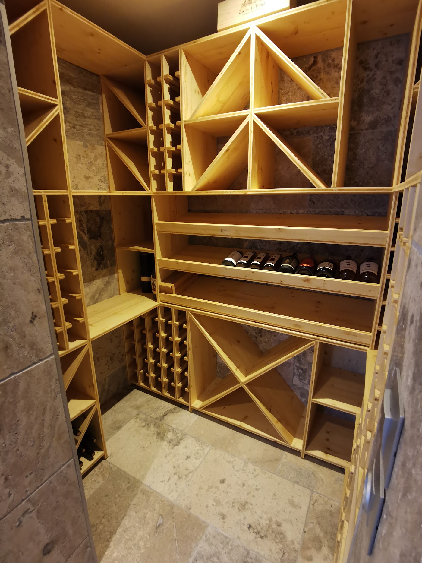 Cave à vin équipée de casiers en croix, d'étagères et d'une niche à bouteilles en bois clair.
